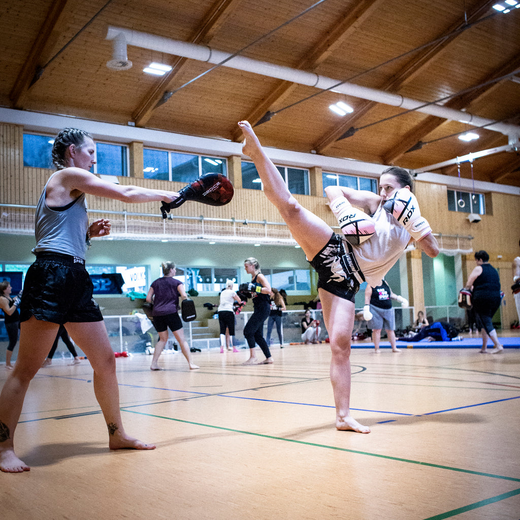 Frauen beim fortgeschrittenen Kickbox Training während einem Chinkilla Camp. Eine Frau im Fokus trägt Chinkilla Fightgear. Women during an advanced kickboxing class at a Chinkilla camp. One woman in the front is wearing Chinkilla fightgear.